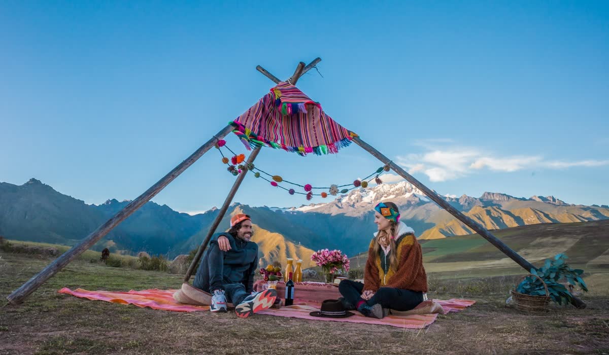 Couple on textiles under a canopy facing snowcapped mountains